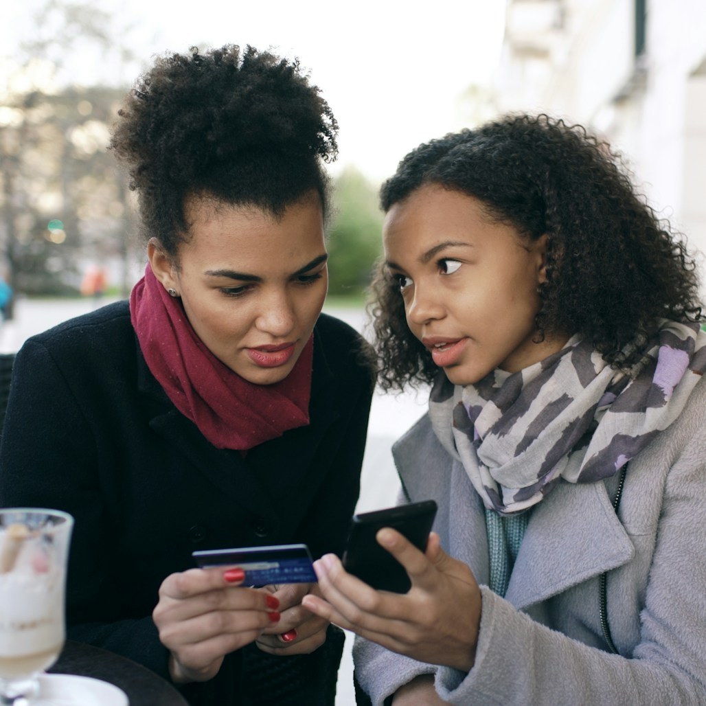 Two friends paying with card and phone